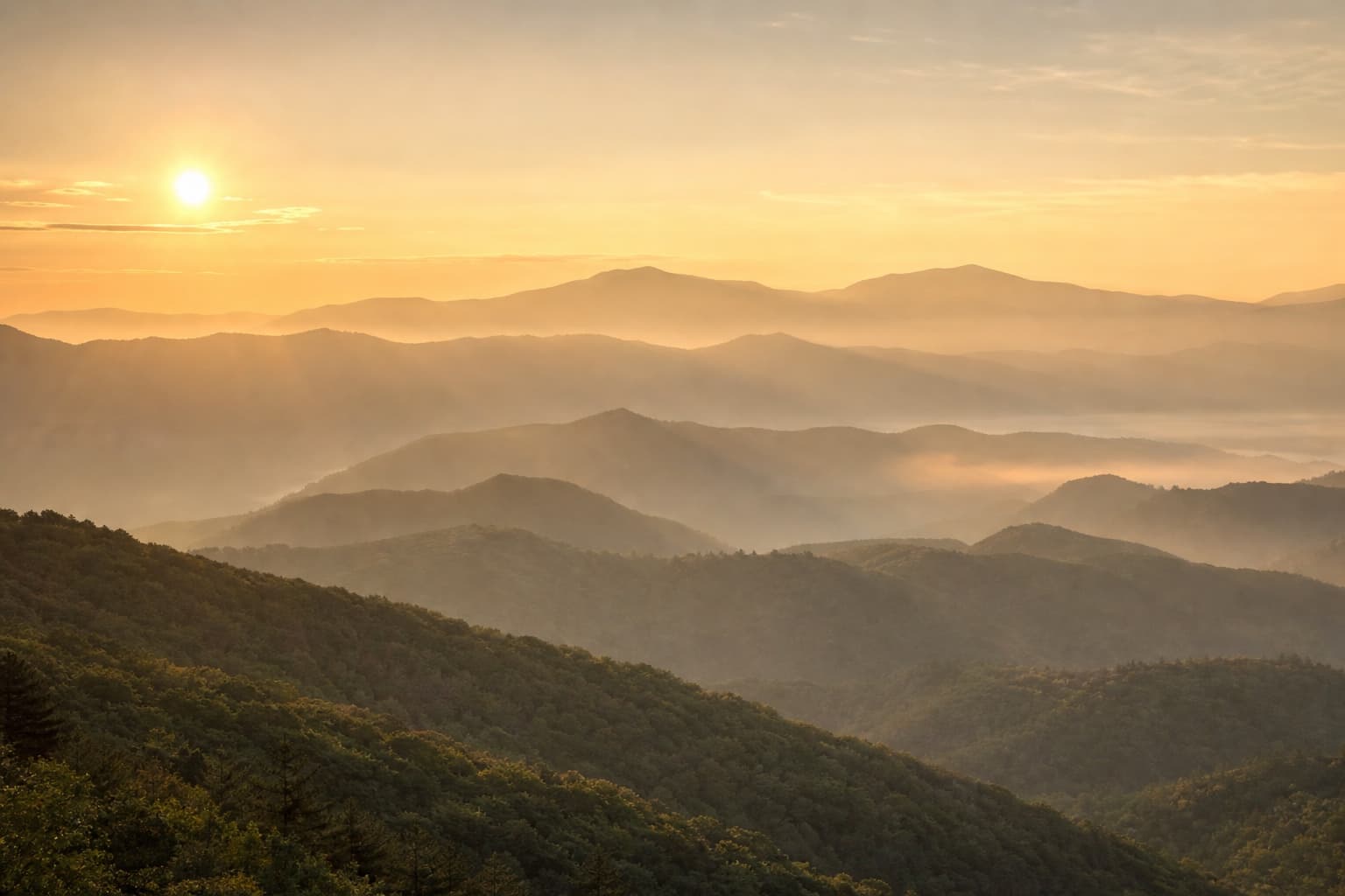 Layered mountain ridgelines fading into warm golden mist at sunrise.